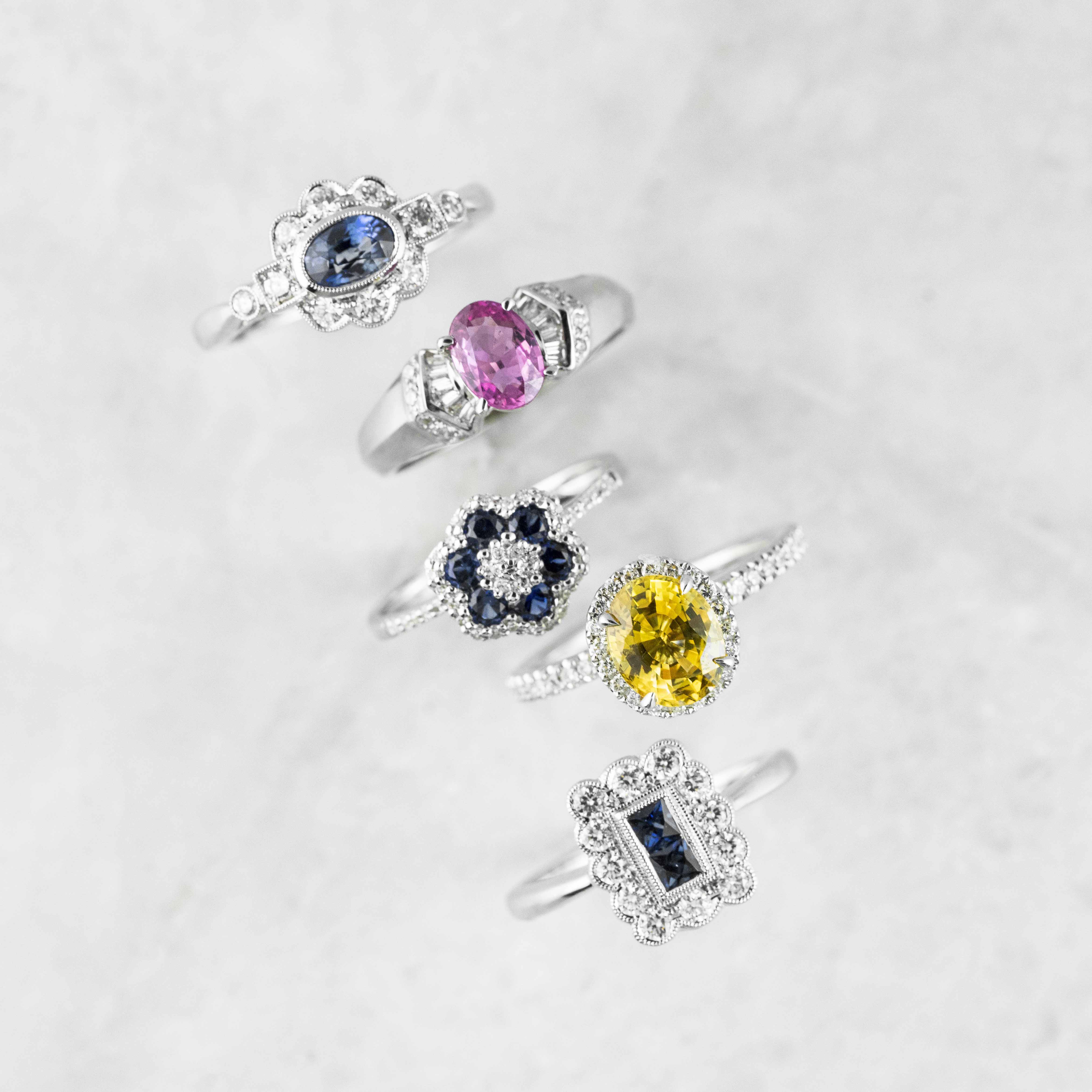 Five white gold engagement rings centered with different colored gemstones.
