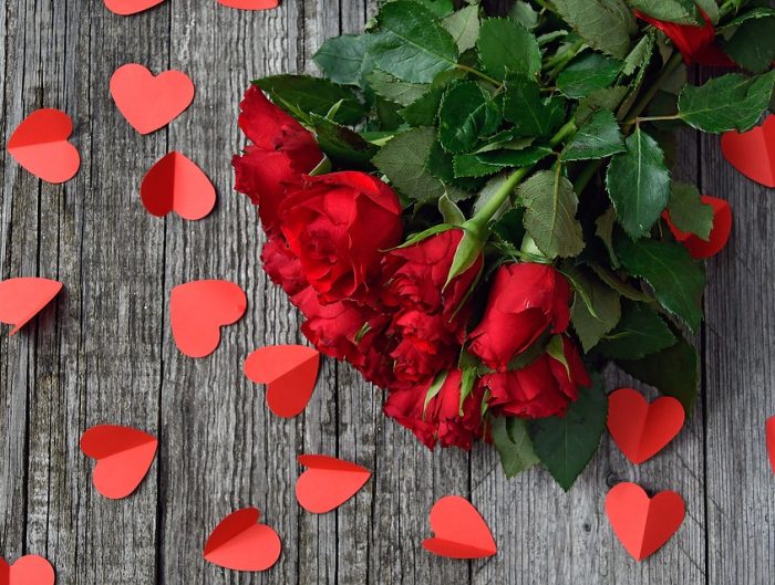 Rose bouquet on wooden plank floor with red paper hearts spread on the floor.