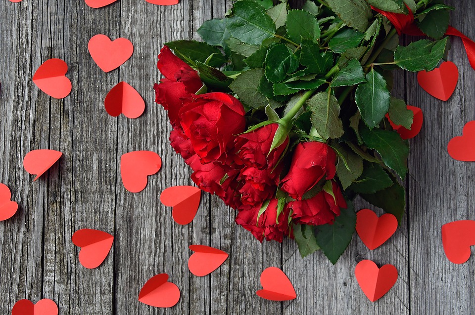 Rose bouquet on wooden plank floor with red paper hearts spread on the floor.