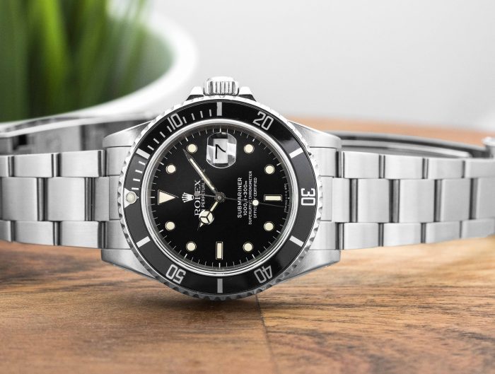 Pre-owned men’s Rolex Deepsea Sea-Dweller in stainless steel with a black dial on a wooden table.