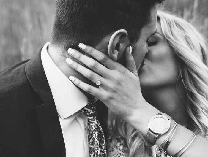 Bride and groom kissing featuring woman’s hand with diamond engagement ring.