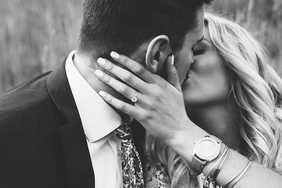 Bride and groom kissing featuring woman’s hand with diamond engagement ring.