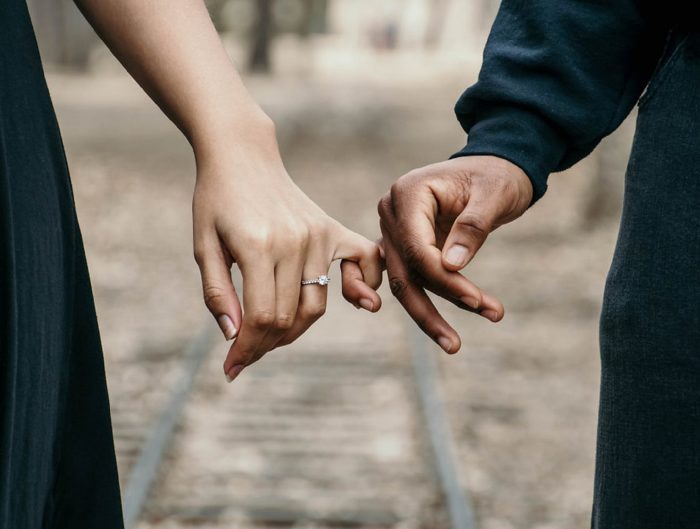 Couple holding hands showing of woman’s diamond engagement ring.