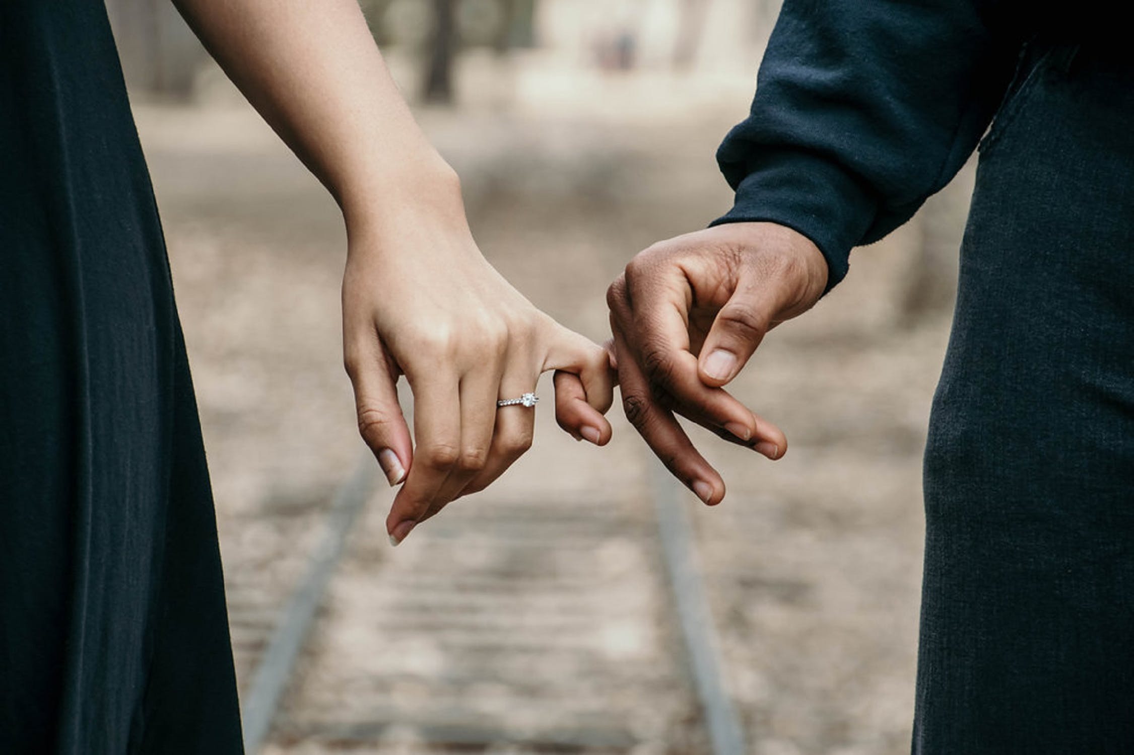 Couple holding hands showing of woman’s diamond engagement ring.