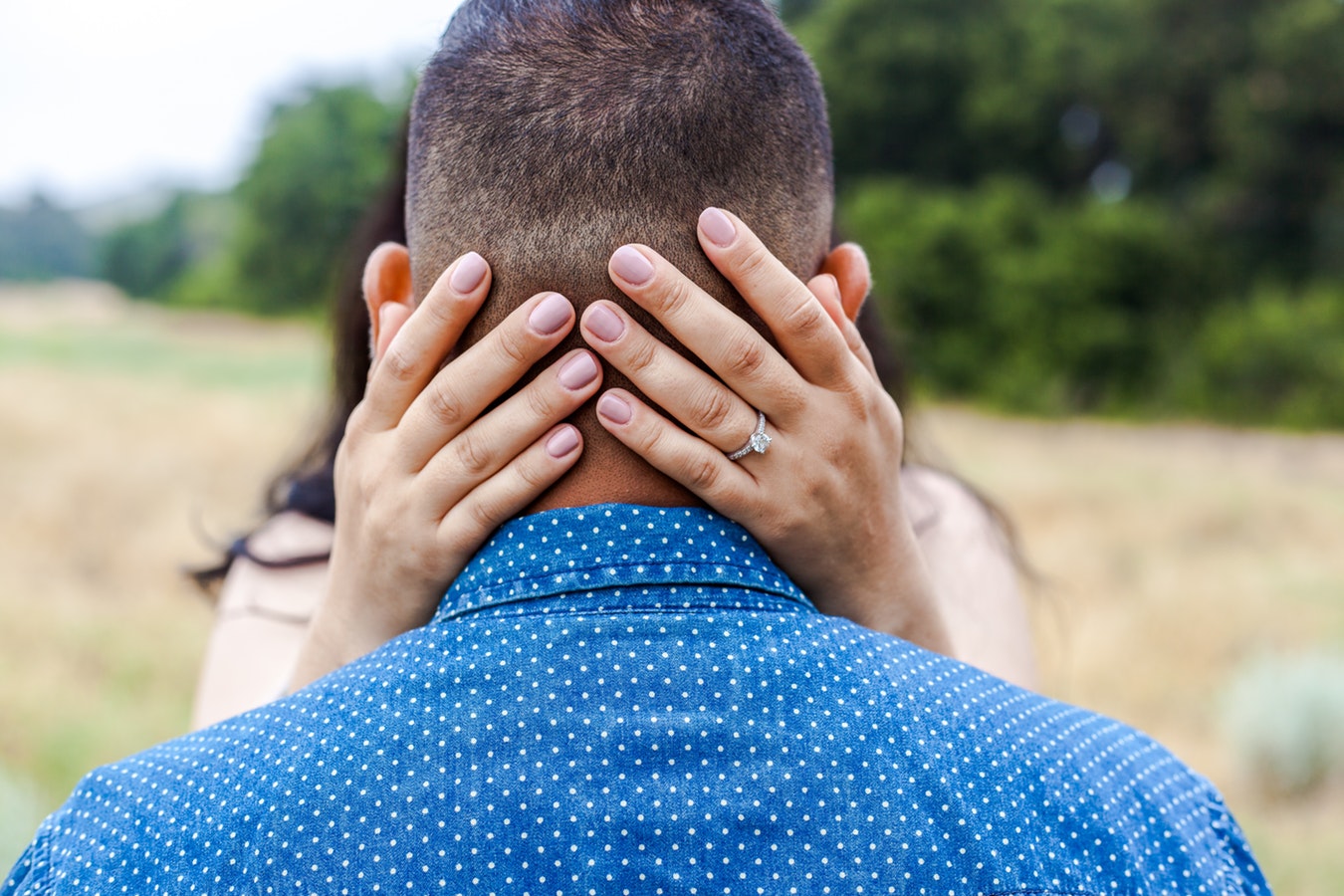 Woman’s hands on back of man’s head featuring her diamond engagement ring.
