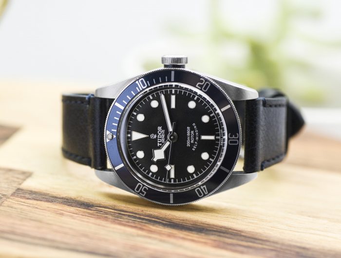 Pre-owned men’s Tudor in stainless steel with a black leather strap on a wooden table.