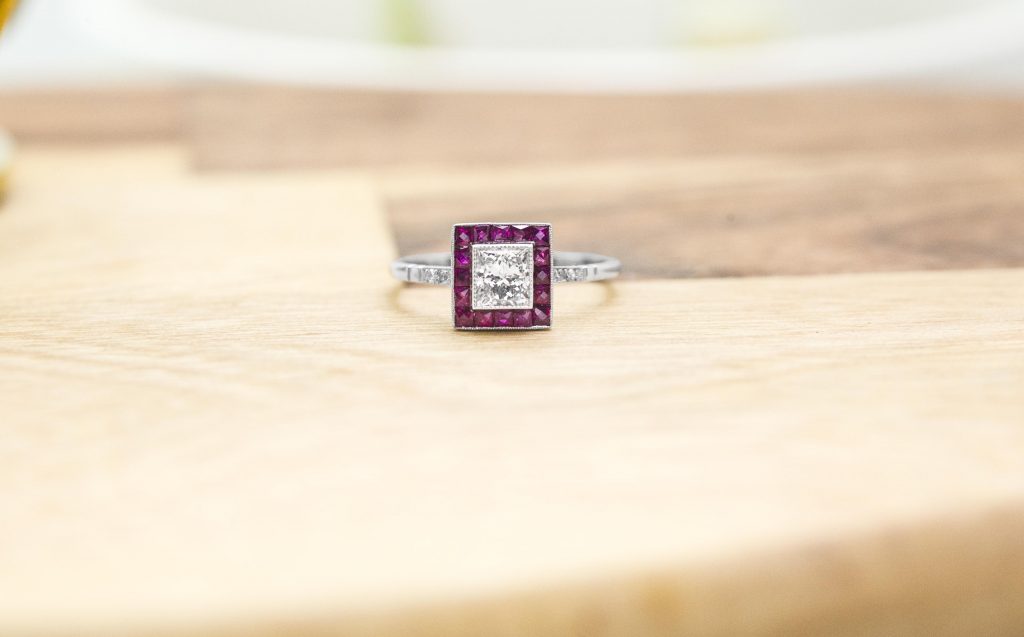 White gold diamond engagement ring with a ruby halo and diamonds in the band.