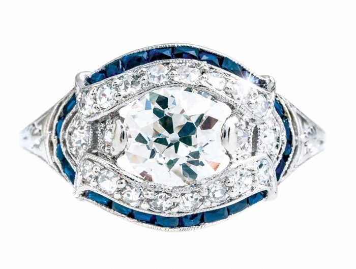 White gold diamond engagement ring surrounded by a double halo of diamonds and blue sapphires with diamonds in the band.