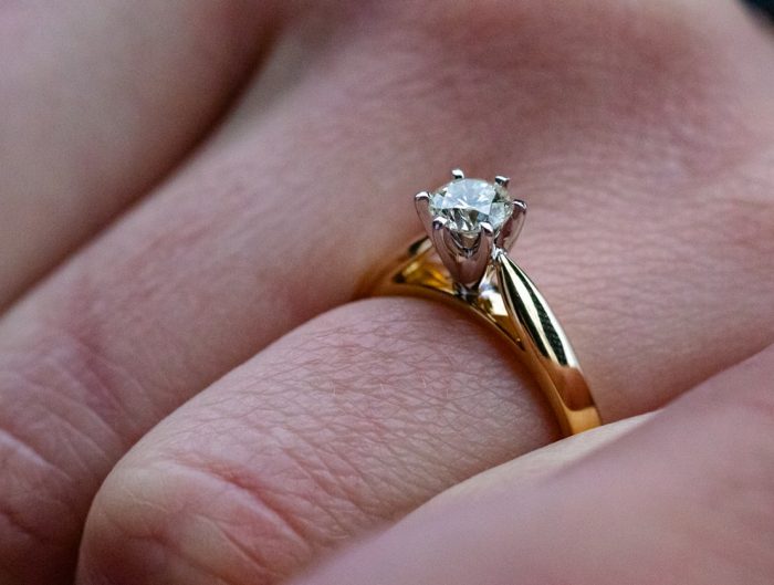 Woman’s hand with yellow gold solitaire cathedral diamond engagement ring.