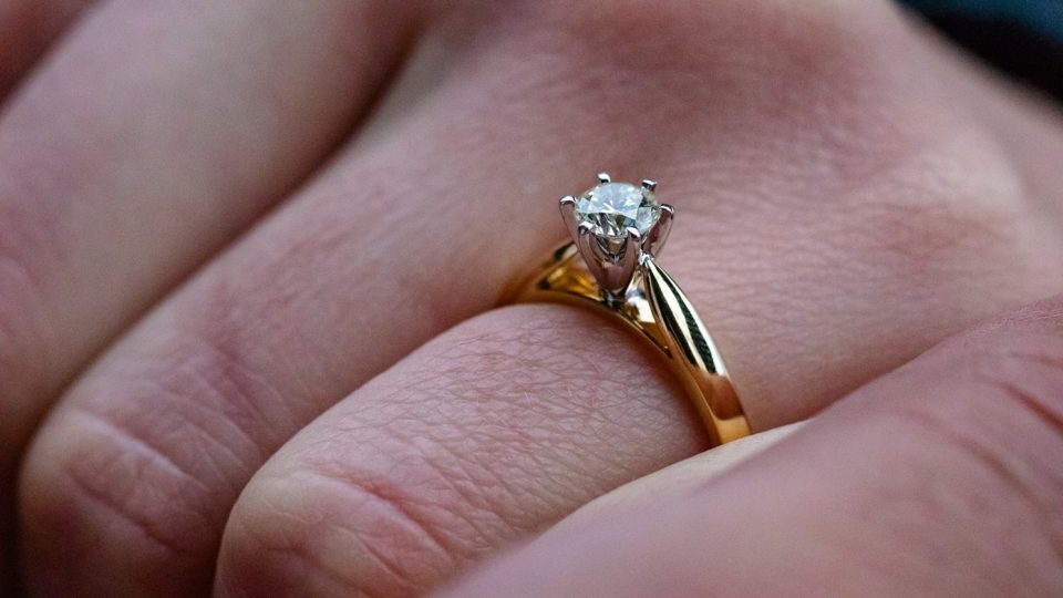 Woman’s hand with yellow gold solitaire cathedral diamond engagement ring.