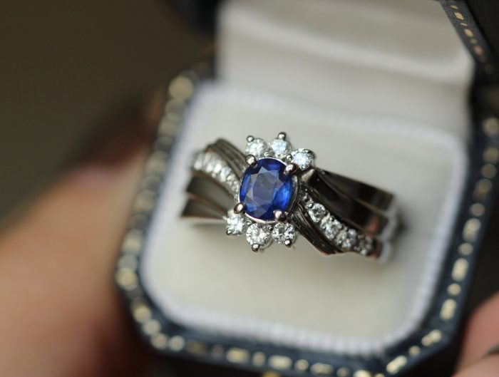 White gold engagement ring centered with a blue sapphire surrounded by a half-halo of diamond and diamonds in the band.