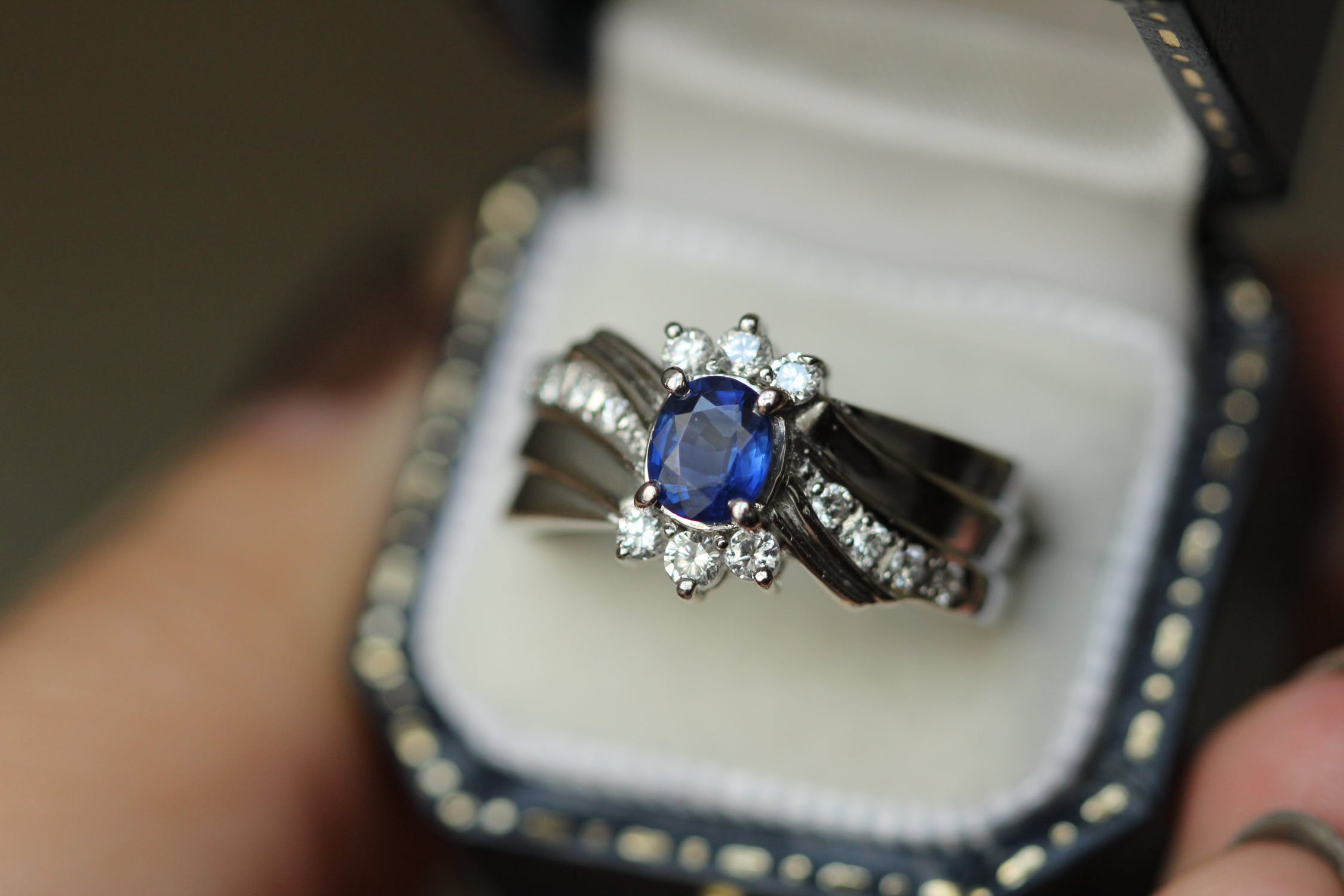 White gold engagement ring centered with a blue sapphire surrounded by a half-halo of diamond and diamonds in the band.