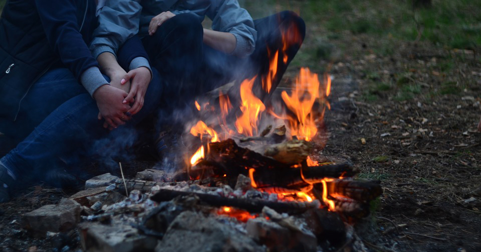 Man and woman embracing next to campfire.