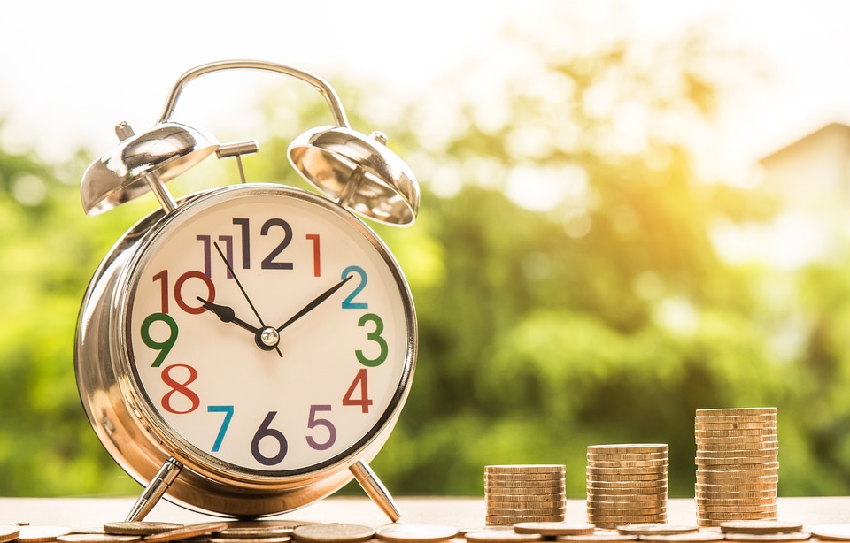 Alarm clock next to stacks of gold coins.