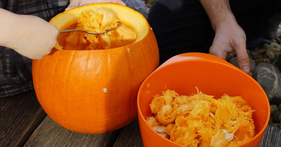 Person scooping out the insides of a pumpkin to carve.