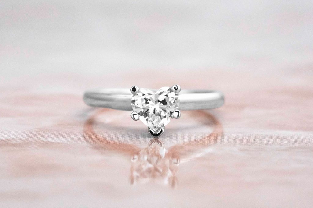 White gold solitaire diamond engagement ring on pink marble table.