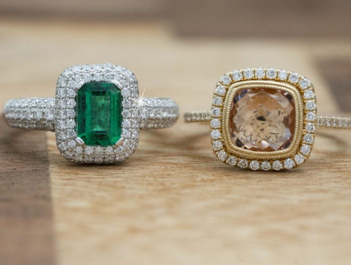 Two engagement rings centered with gemstones on a wooden table.