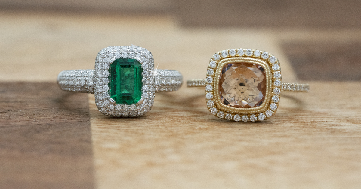 Two engagement rings centered with gemstones on a wooden table.