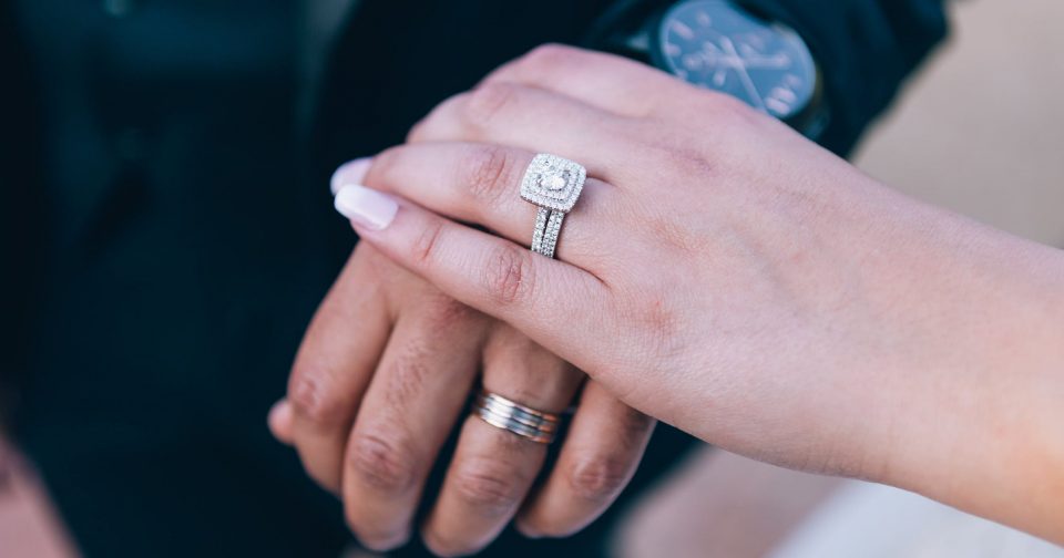 Bride and groom holding hands showing off her diamond wedding set and his white gold wedding band.