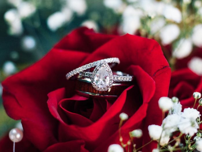 White gold diamond engagement ring and diamond wedding band in center of a red rose.