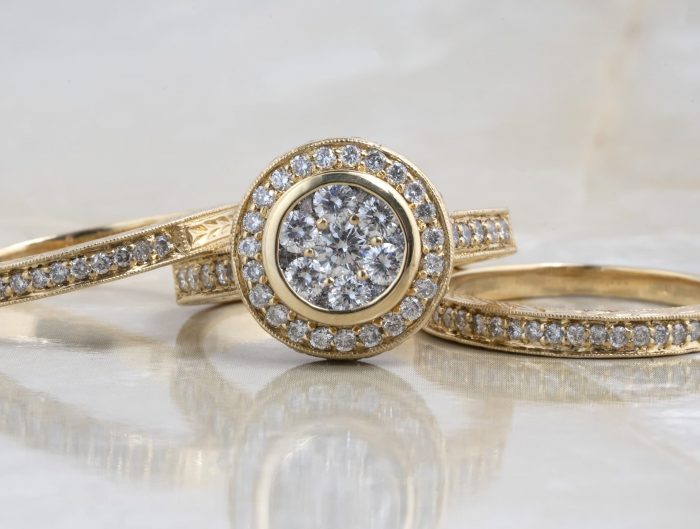 Yellow gold diamond engagement ring with matching diamond wedding bands on a marble table.