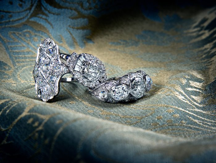 Antique platinum filigree diamond rings on blue and gold fabric background.