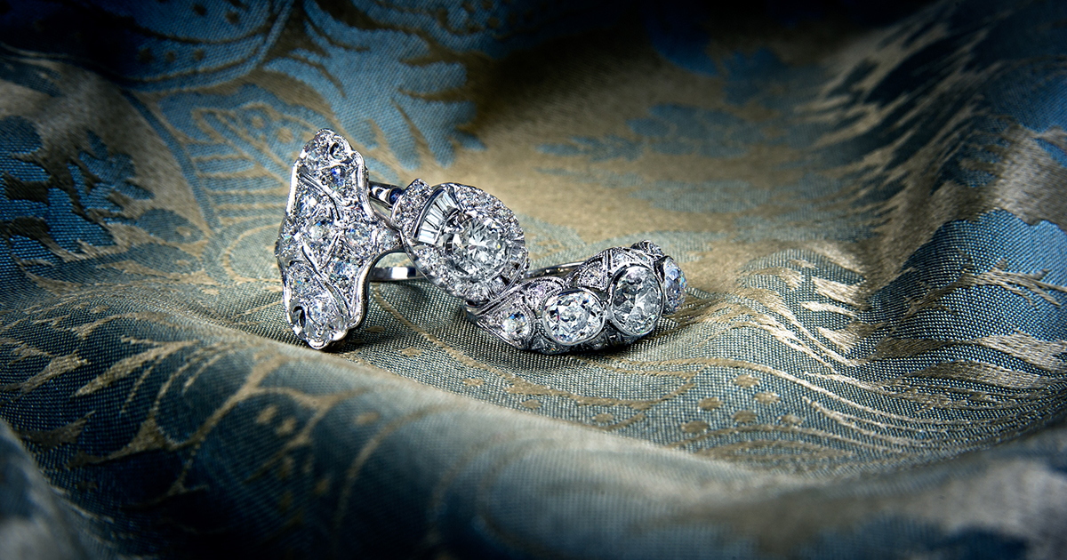 Antique platinum filigree diamond rings on blue and gold fabric background.