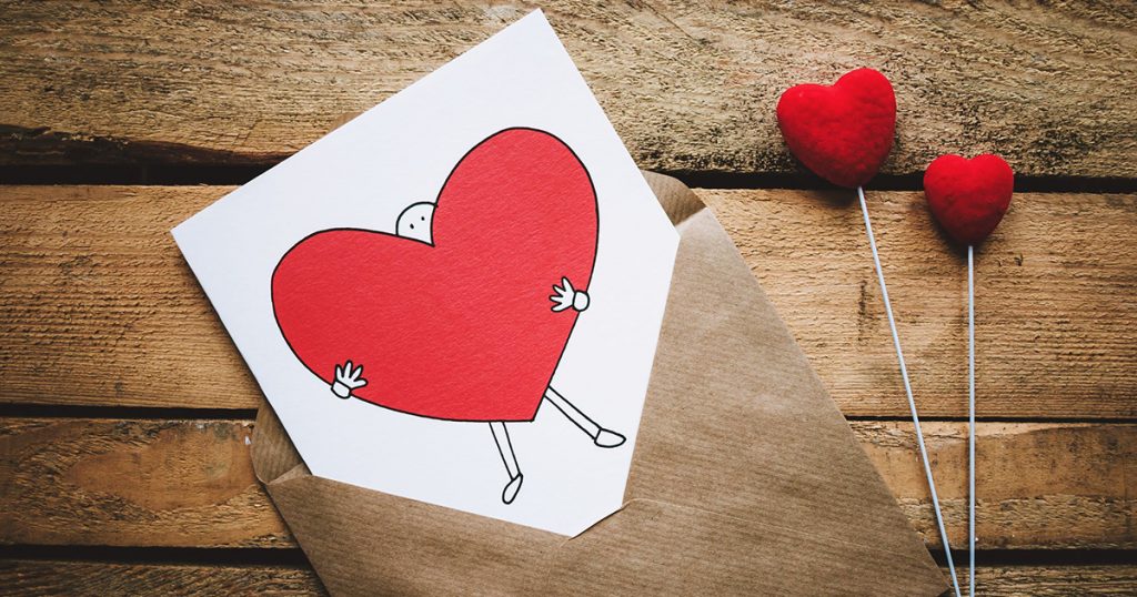 Red heart Valentine’s Day card on wooden table.