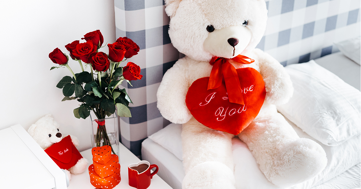 Valentine’s Day teddy bear and vase of red roses on nightstand.