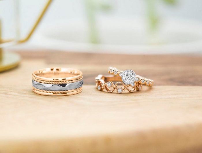 Yellow gold diamond engagement ring, yellow gold diamond eternity band, and men’s yellow and white gold wedding band on wooden table.