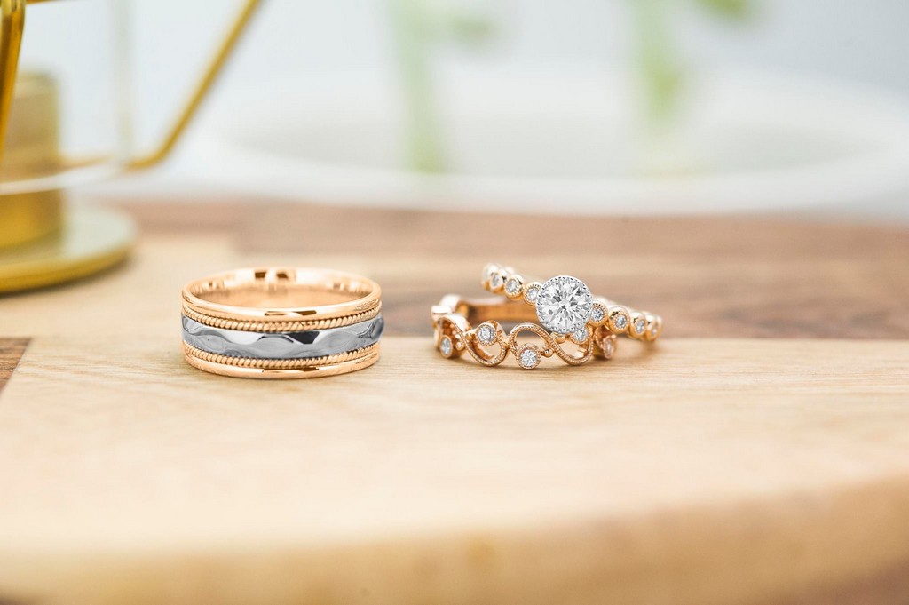 Yellow gold diamond engagement ring, yellow gold diamond eternity band, and men’s yellow and white gold wedding band on wooden table.