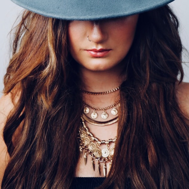 Woman in hat wearing chunky layered necklaces.