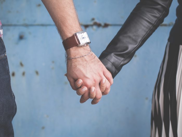 Couple holding hands in front of blue backdrop.