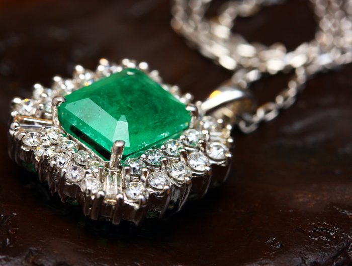 Antique white gold pendant centered with an emerald surrounded by a double diamond halo.