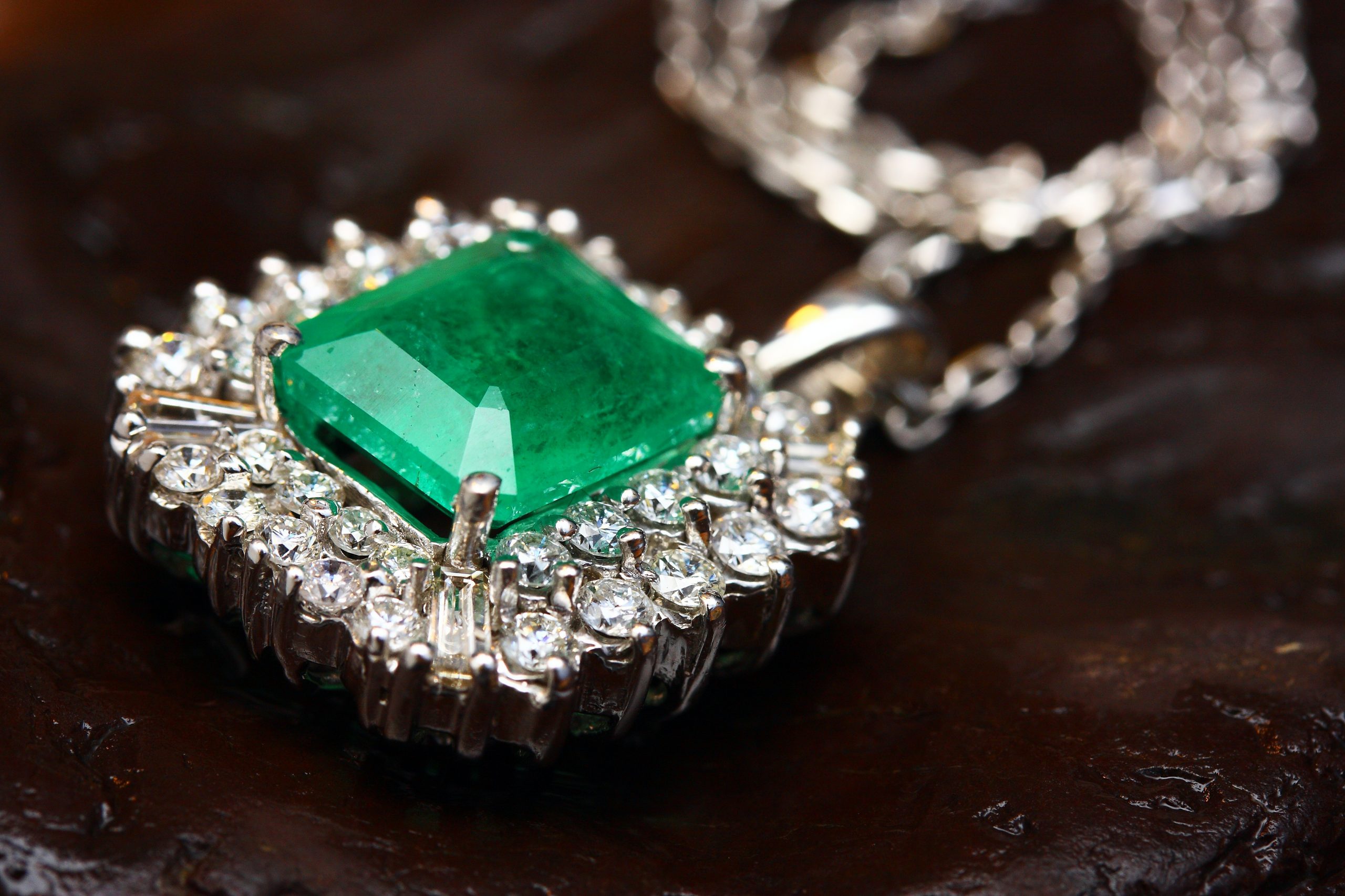 Antique white gold pendant centered with an emerald surrounded by a double diamond halo.
