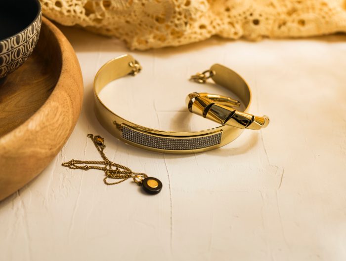 Stacked pieces of yellow gold jewelry on beige countertop.