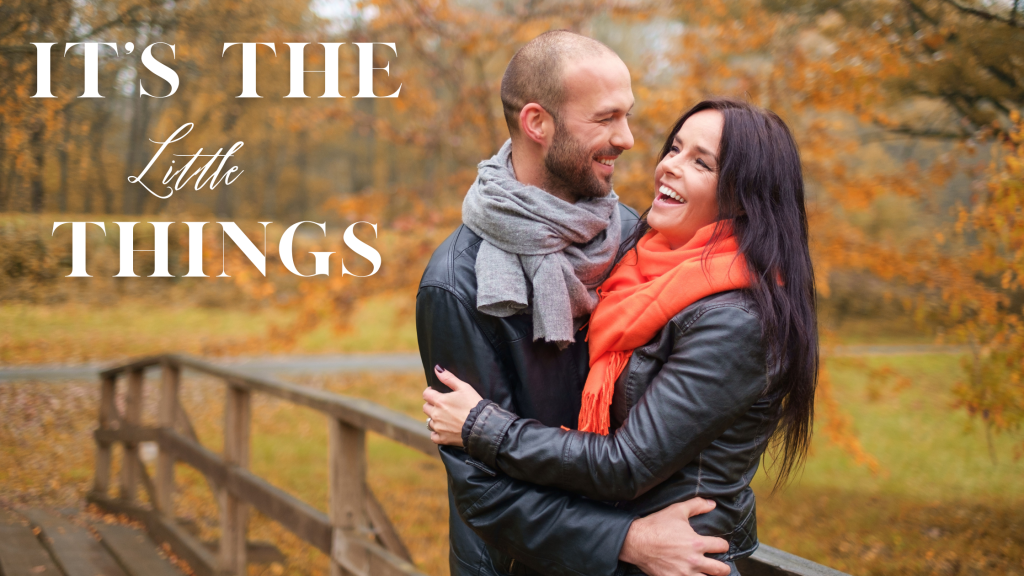 Couple embracing on walking bridge in field with text “It’s the Little Things”.