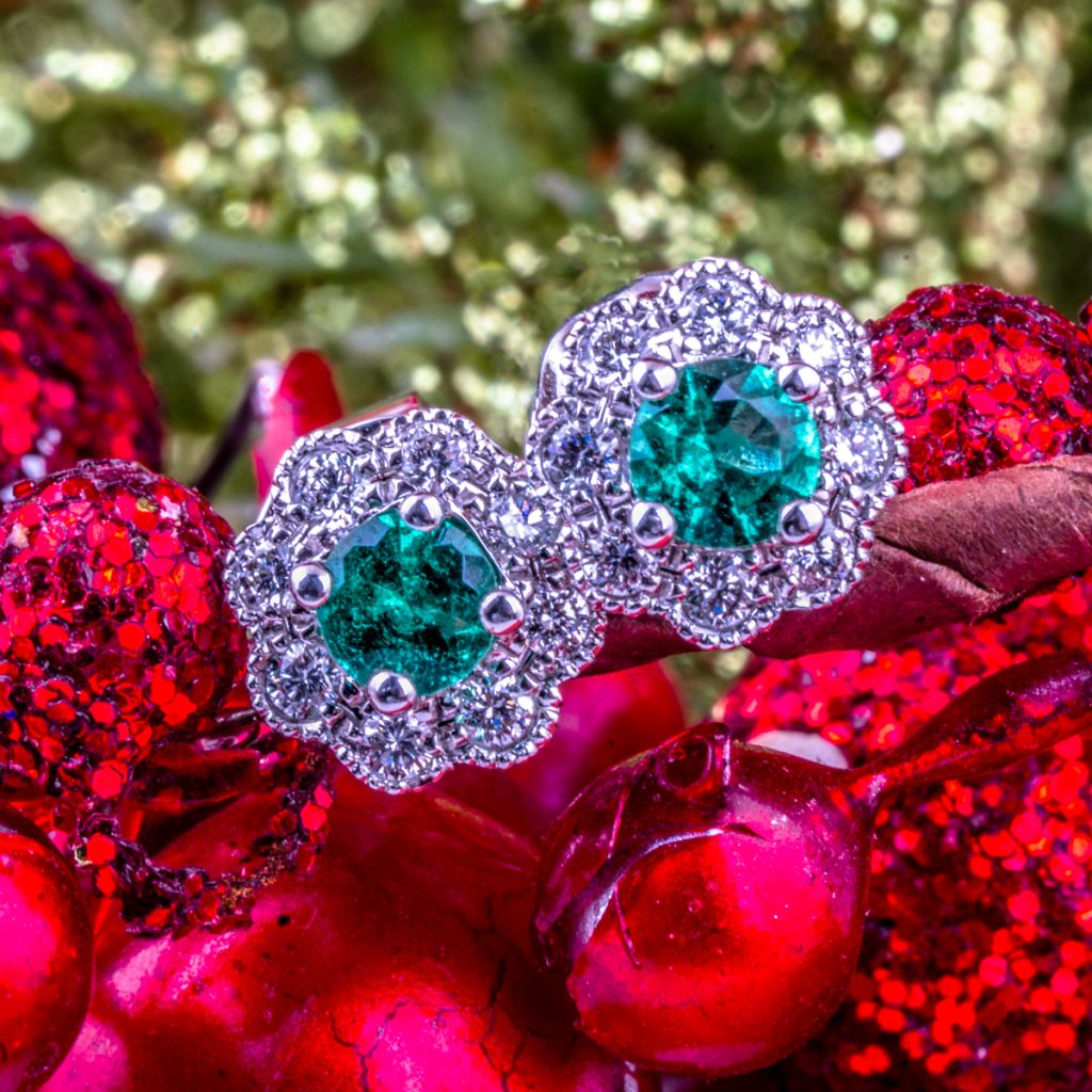 New diamond and emerald flower stud earrings on a red tinsel background.