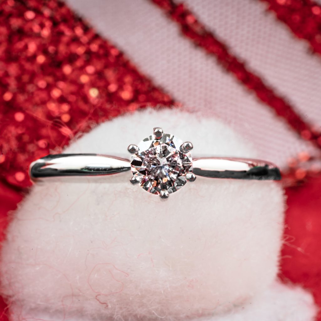 Vintage white gold solitaire diamond engagement ring displayed on a white pouf.