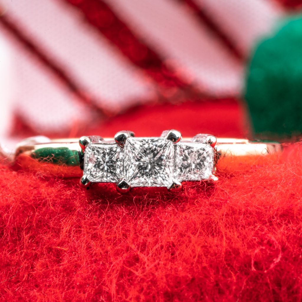 Vintage yellow gold three-stone diamond engagement ring on a red cloth background.