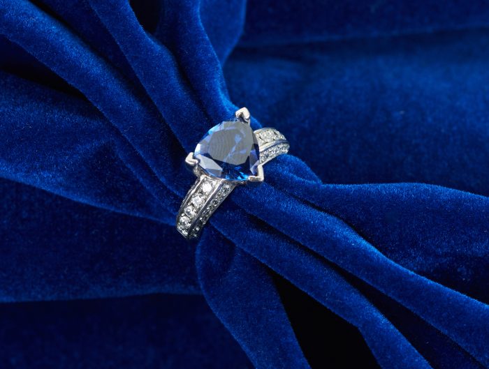 White gold engagement ring centered with a trillion cut blue sapphire and diamonds in the band.