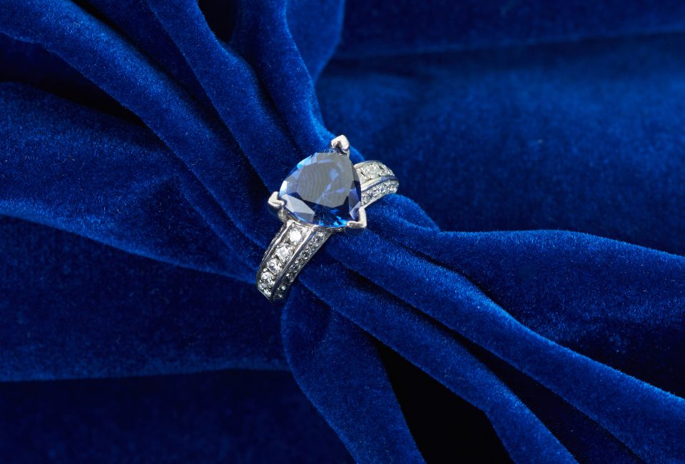 White gold engagement ring centered with a trillion cut blue sapphire and diamonds in the band.