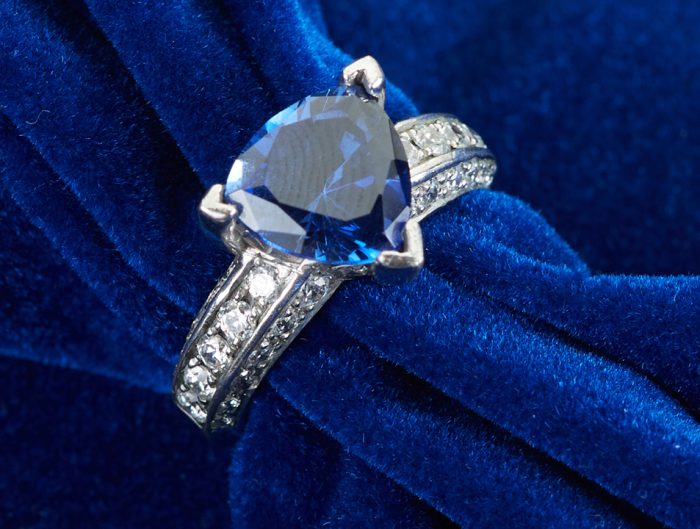 White gold engagement ring centered with a trillion cut blue sapphire and diamonds in the band.