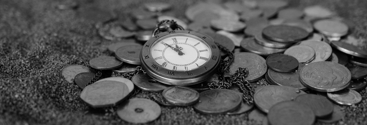 Antique pocket watch surrounded by a pile of collectible coins.