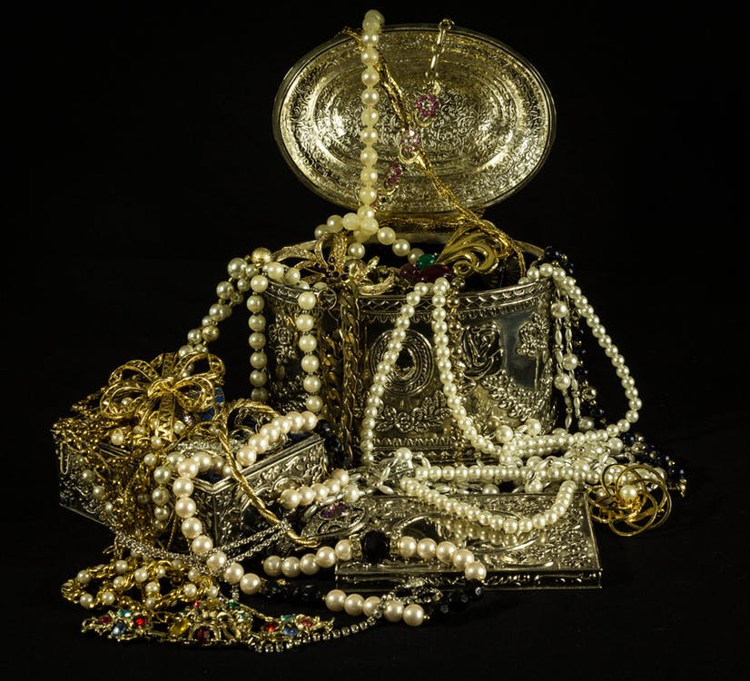 Antique jewelry box overflowing with vintage jewelry including pearl strands and brooches.