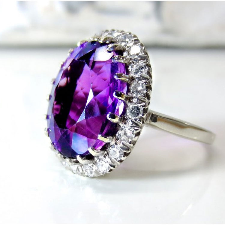 White gold ring centered with a purple gemstone surrounded by a diamond halo.