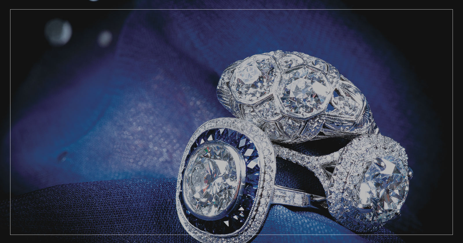 Three diamond and gemstone rings on a blue fabric background.