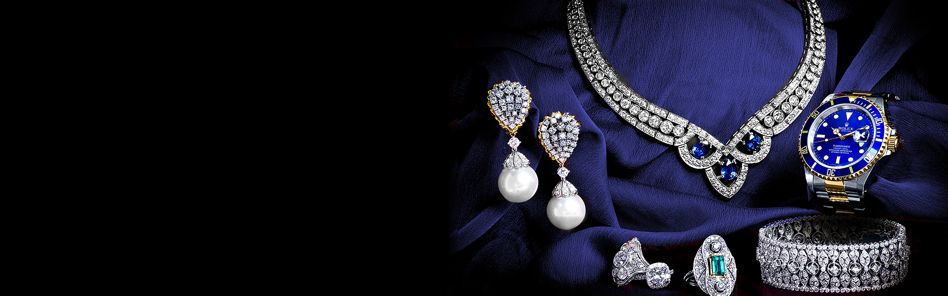 A pair of pearl earrings, a diamond necklace, a rolex watch and other jewelry lying on top of a blue cloth.
