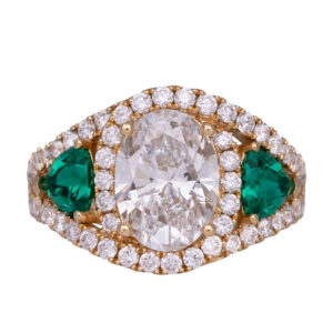 yellow gold halo ring centered with an oval diamond flanked by trillion emeralds and surrounded by round brilliant diamonds