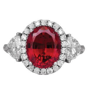white gold halo ring centered with an oval ruby surrounded by round diamonds flanked by trillion cut diamonds